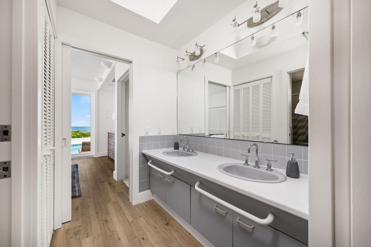 A modern bathroom with two sinks, a large mirror, and a view of the outdoors.