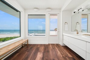 A bathroom with a wooden floor, white cabinets, a bench, and a large window with a view of the beach. - Panoramic Paradise I Luxury Beachfront Estate & Boardwalk to the Beach (Saint Augustine)