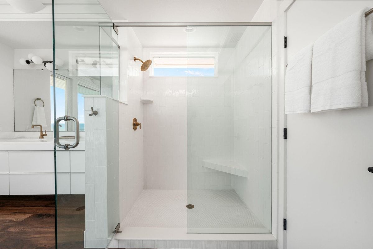 A modern bathroom with a glass-enclosed shower, white tiles, and a visible window.