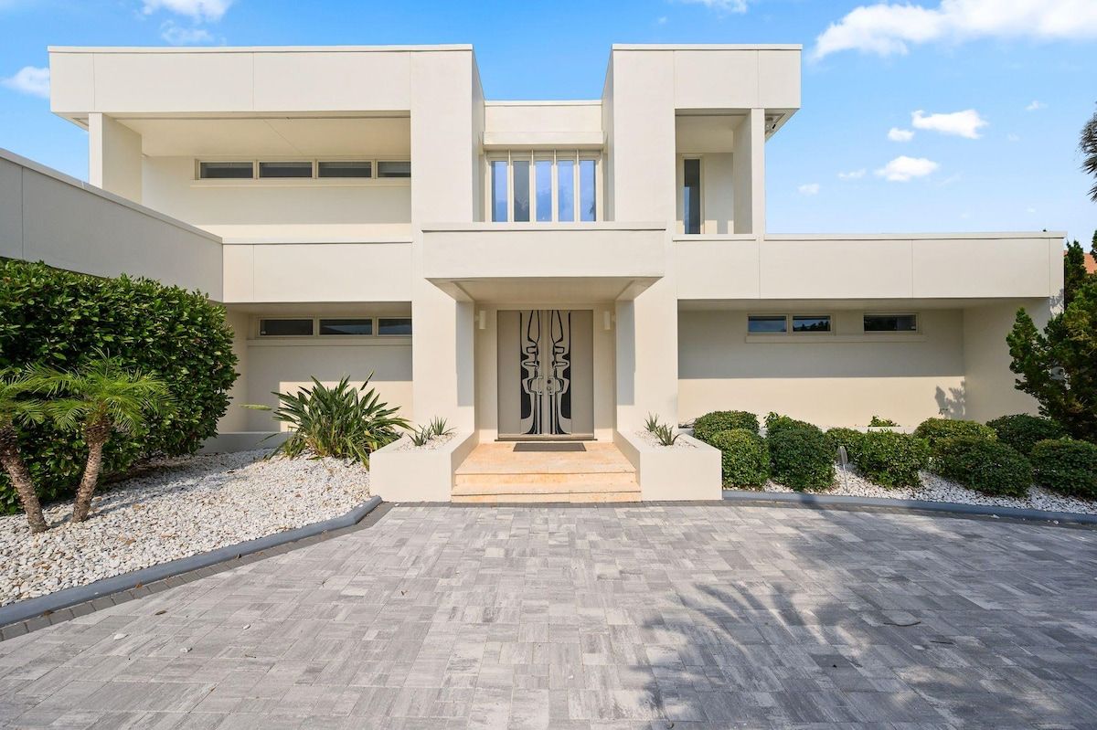 A modern building with a symmetrical facade, a central entrance with a decorative door, and a paved driveway.