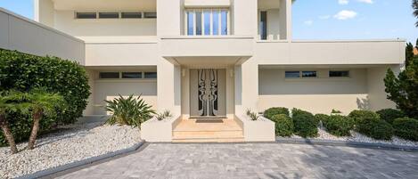 A modern building with a symmetrical facade, a central entrance with a decorative door, and a paved driveway.