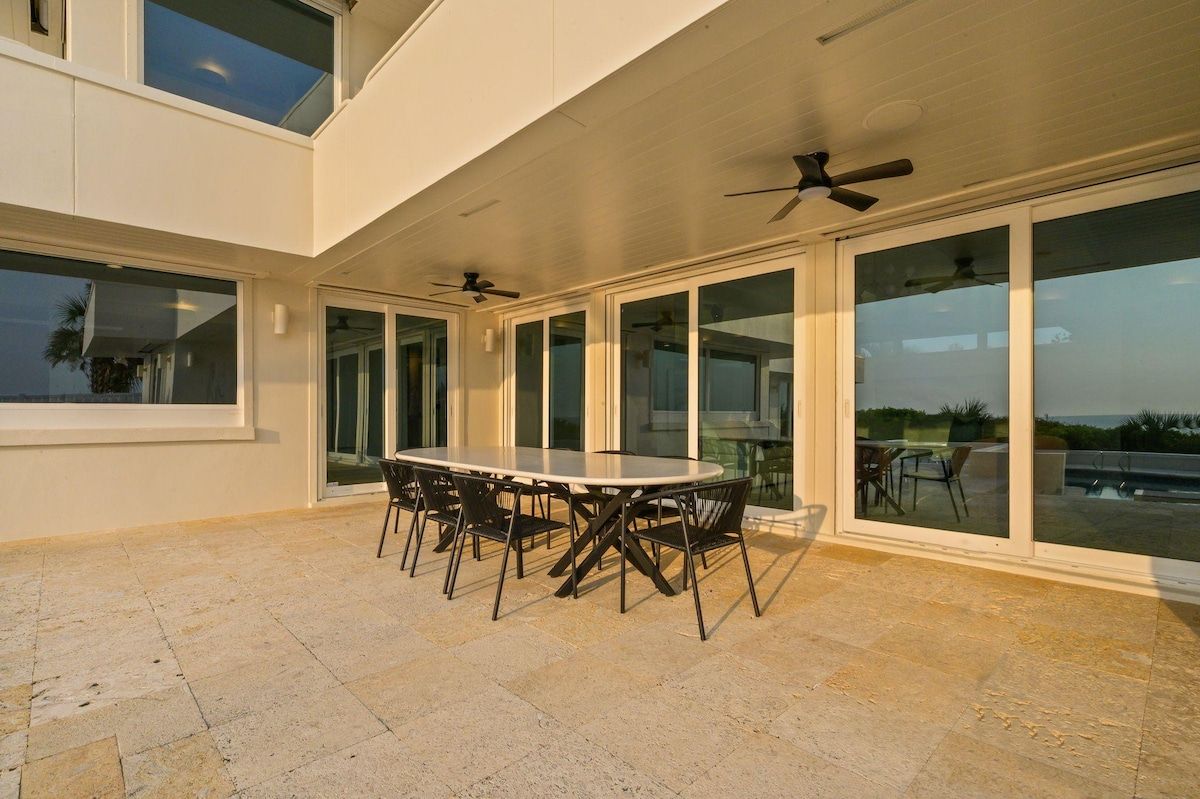 A covered outdoor patio with a round table and chairs, large sliding glass doors, and ceiling fans.