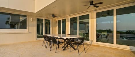 Une terrasse extérieure couverte, dotée d’une table ronde et de chaises, de grandes portes-fenêtres coulissantes et de ventilateurs de plafond.