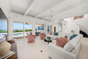 A spacious living room with a white ceiling, a large window overlooking a pool, and a staircase leading to another level. - Panoramic Paradise I Luxury Beachfront Estate & Boardwalk to the Beach (Saint Augustine)