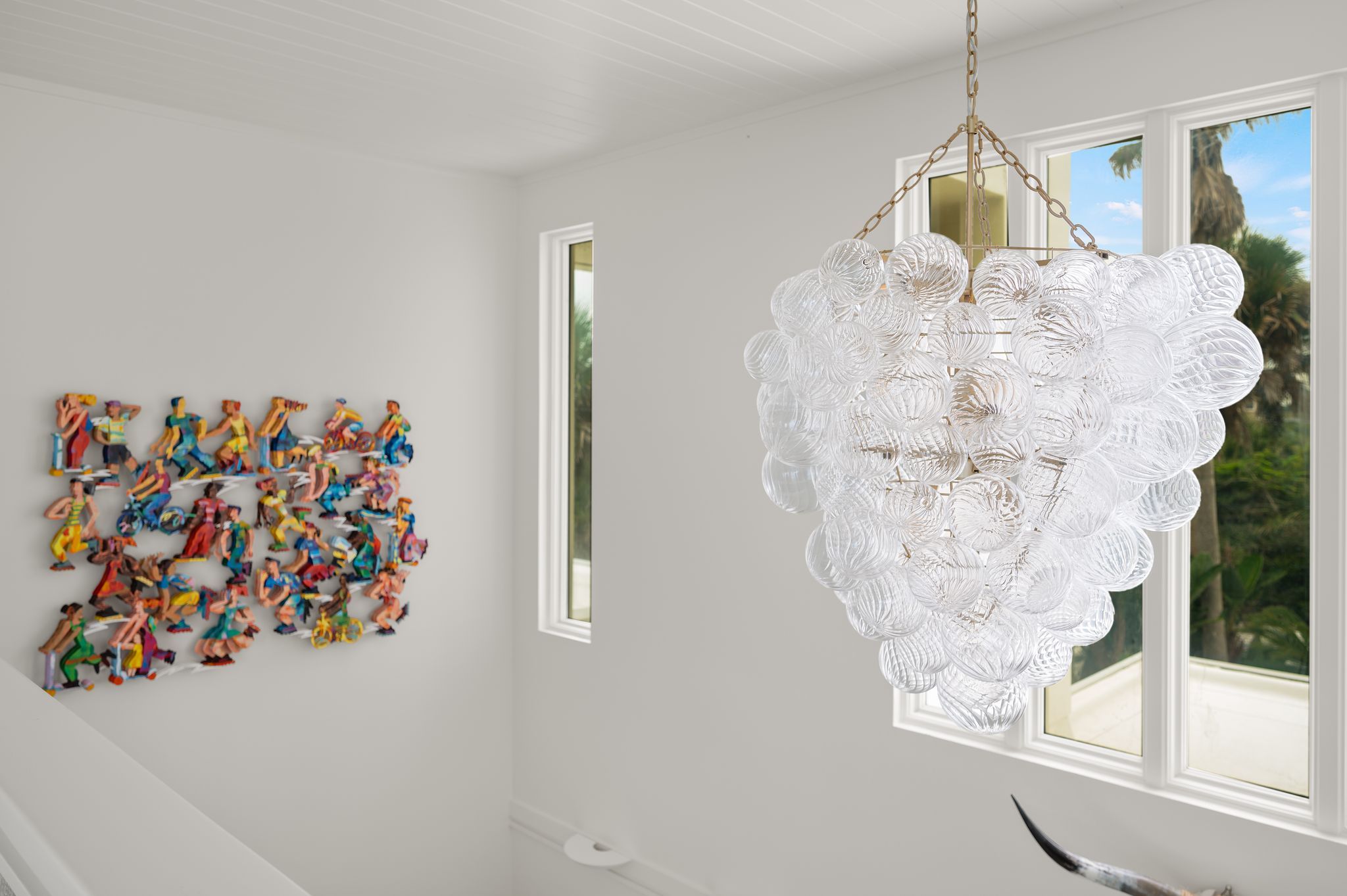 Une pièce dotée d’un escalier, d’une sculpture colorée fixée au mur et d’un lustre unique.