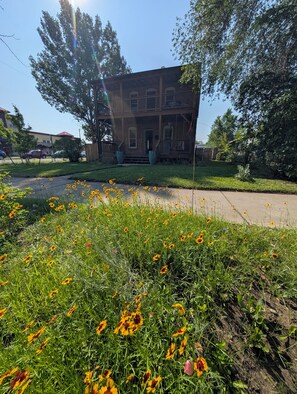 Ein zweistöckiges Backsteingebäude mit Veranda und einem Rasen mit Wildblumen.