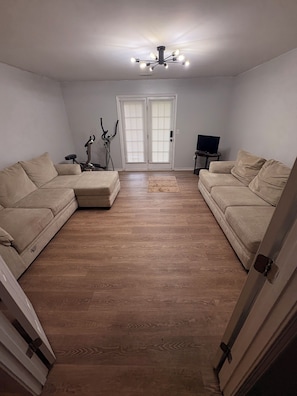 A living room with two beige sofas, a wooden floor, a ceiling fan, and a door with blinds. - Cozy 1-bedroom house in superb Conyers with AC (Conyers)