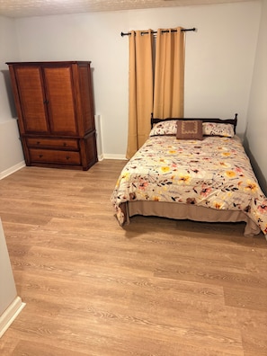A bedroom with a wooden wardrobe, a bed with floral bedding, and a window with beige curtains. - Cozy 1-bedroom house in superb Conyers with AC (Conyers)