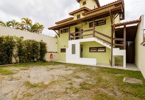 Ein zweistöckiges Haus mit einer Treppe, die zu dem oberen Stockwerk führt, einem kleinen Garten mit Gras und Kies sowie einer mit Kletterpflanzen bewachsenen Mauer.
