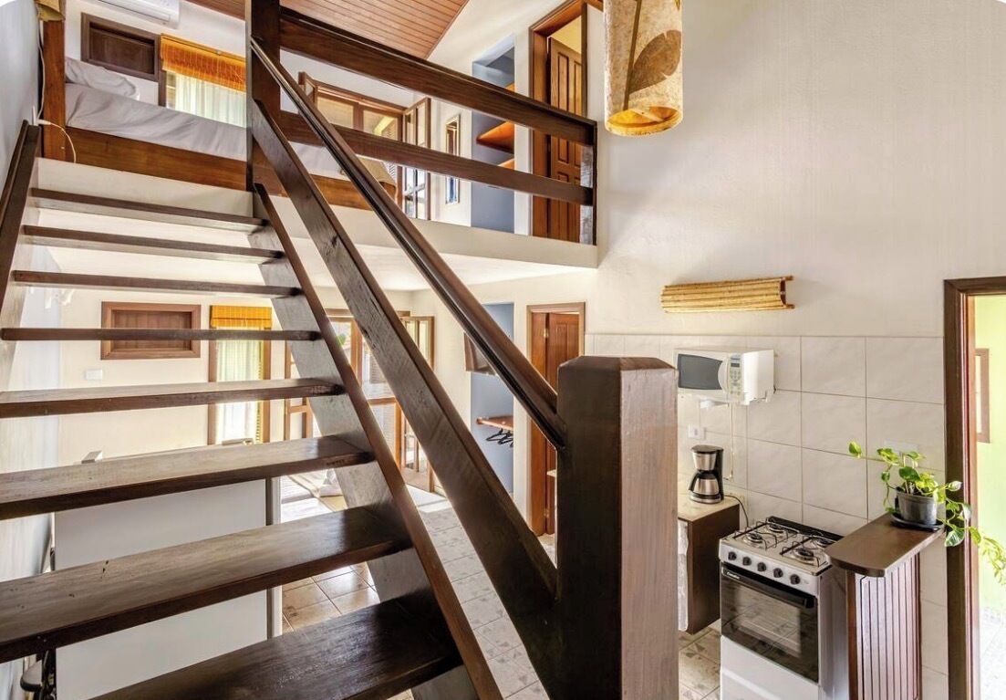A multi-level interior with a wooden staircase, a kitchen area with a stove, and a hanging light fixture.
