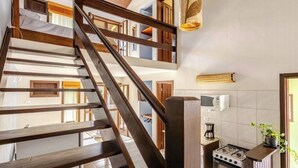 A multi-level interior with a wooden staircase, a kitchen area with a stove, and a hanging light fixture. - Charming loft with a mezzanine, 2 balconies, and 2 bathrooms (são sebastião)