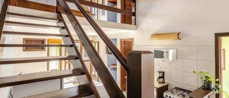 A multi-level interior with a wooden staircase, a kitchen area with a stove, and a hanging light fixture.