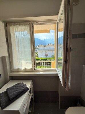 A small bathroom with a window, a washing machine, and a toilet. - Stylish Apartment in Arco, North Garda Lake – Private Garage, Balcony & A/C (Riva del Garda)