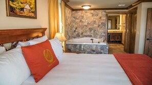Camera d'albergo con un ampio letto, una parete in pietra, un bagno con vasca e un quadro appeso al muro.