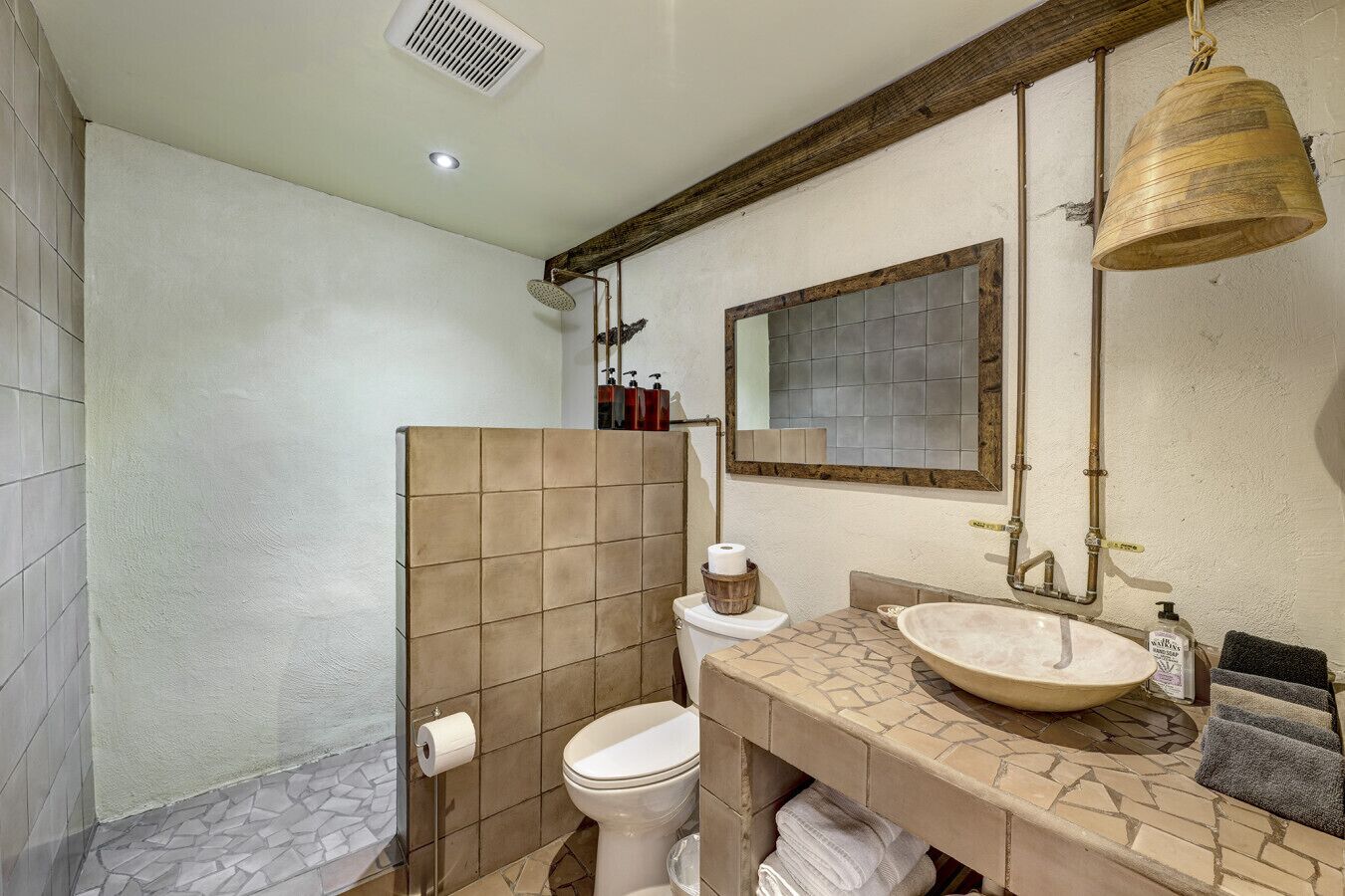 Un baño con ducha, inodoro, lavabo y una campana colgante.