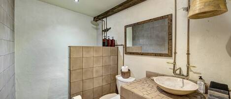 Un baño con ducha, inodoro, lavabo y una campana colgante.