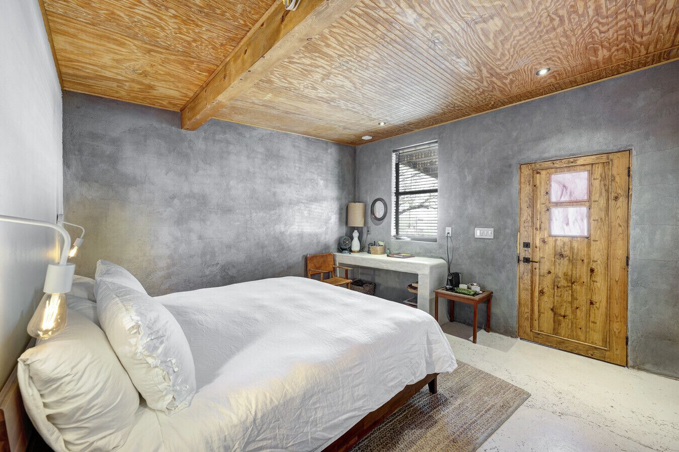 A bedroom with a bed, bedside table, lamp, and a wooden door.
