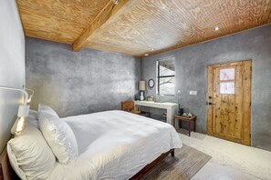 A bedroom with a bed, bedside table, lamp, and a wooden door.