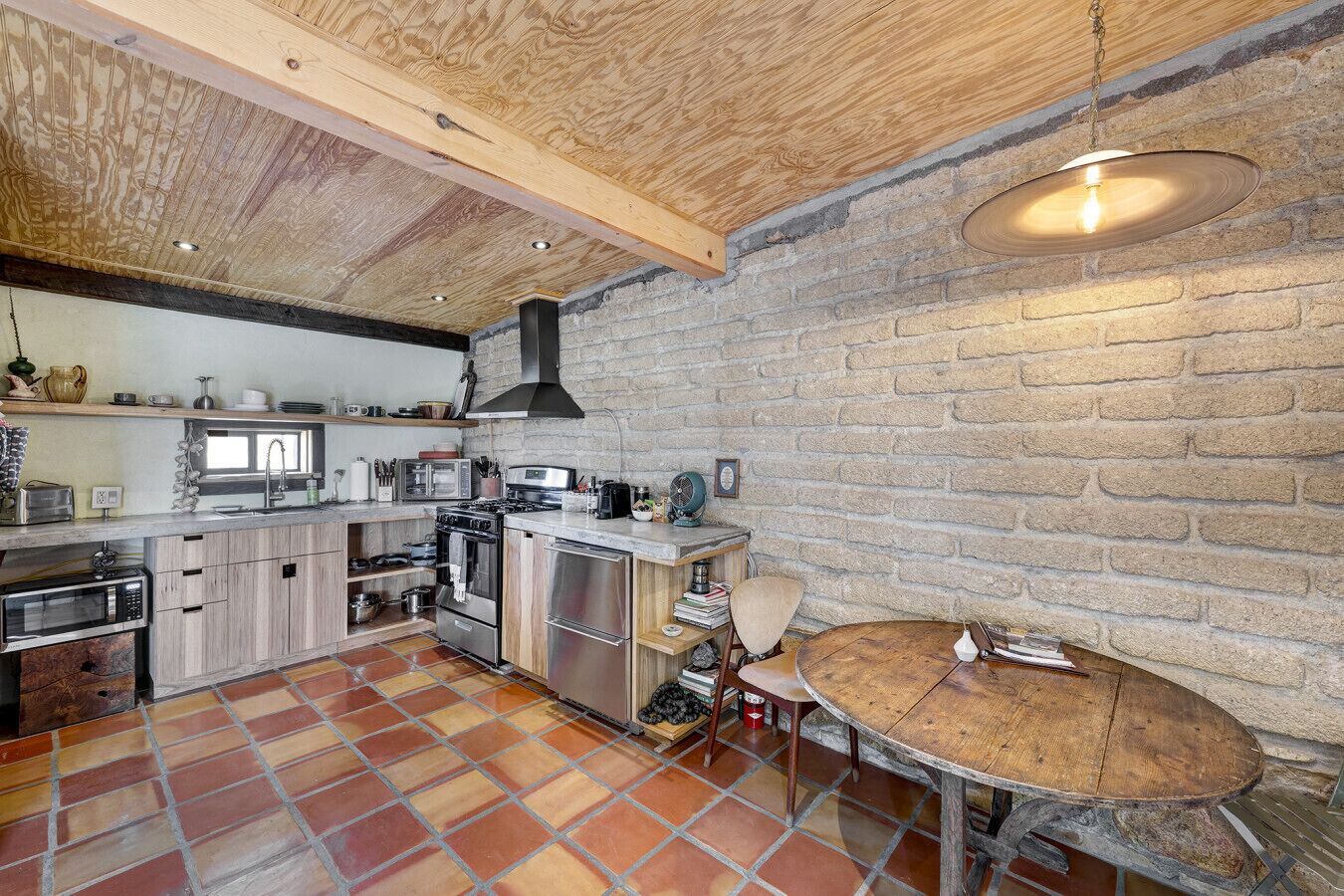 Une cuisine avec un mur en briques, un plafond en bois et une table ronde en bois.