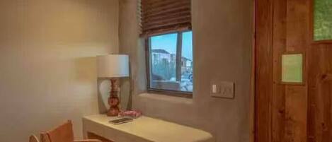 Una habitación con techo de madera, un escritorio con silla, una ventana con persianas y una puerta con un letrero.
