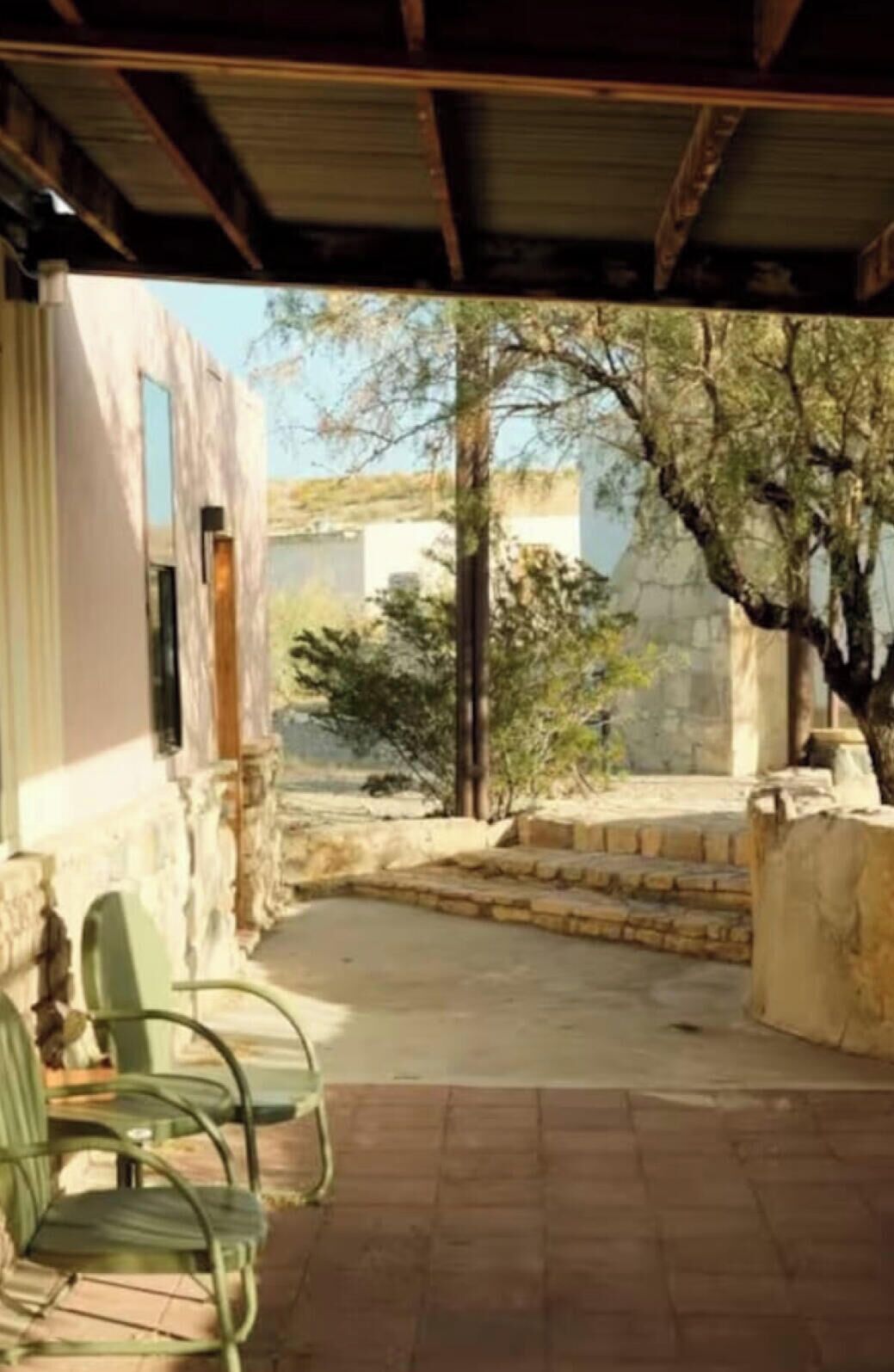 A covered outdoor area with a stone wall, a tree, and a view of a building in the background.