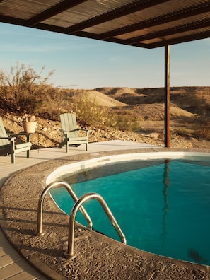 A swimming pool with a metal ladder, surrounded by a deck with chairs and a potted plant.