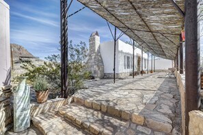 A stone-paved courtyard with steps leading to a white building, a stone tower, and a shaded area with a pergola. - The Study Butte Entire Property (Terlingua)