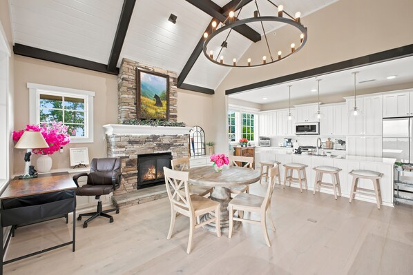 A spacious living area with a fireplace, dining table, and kitchen area with white cabinets and a large island.