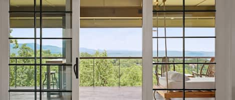 Terraza de madera con vista a un paisaje montañoso a través de un ventanal con celosía metálica.