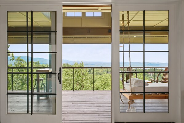 A wooden deck with a view of a mountainous landscape through a glass door with a metal grid.