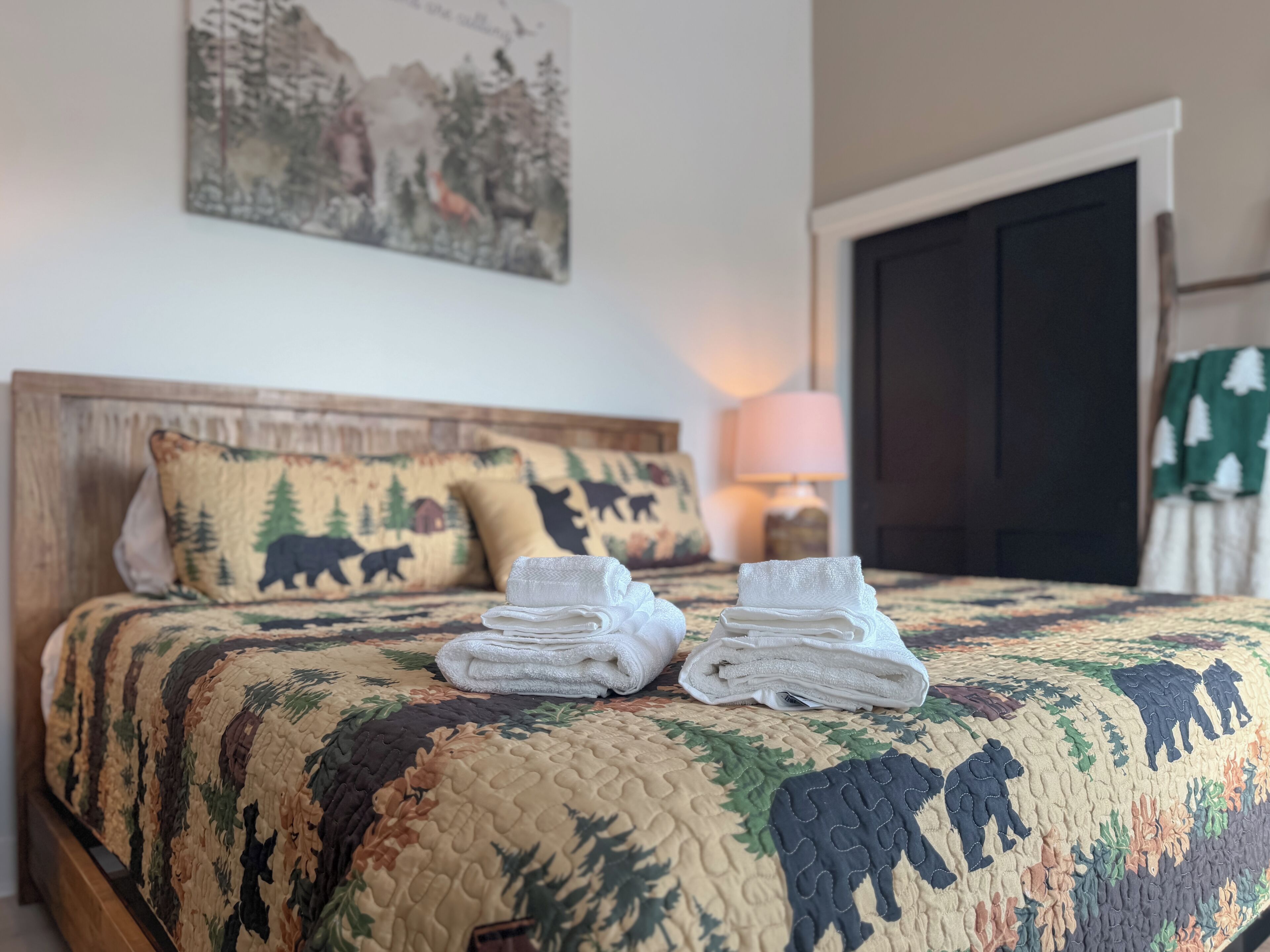 A neatly made bed with a quilt featuring animal prints, a bedside lamp, and a door with a green curtain.