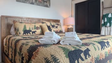 A neatly made bed with a quilt featuring animal prints, a bedside lamp, and a door with a green curtain.