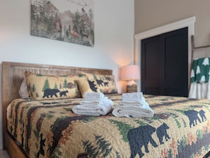 A neatly made bed with a quilt featuring animal prints, a bedside lamp, and a door with a green curtain.