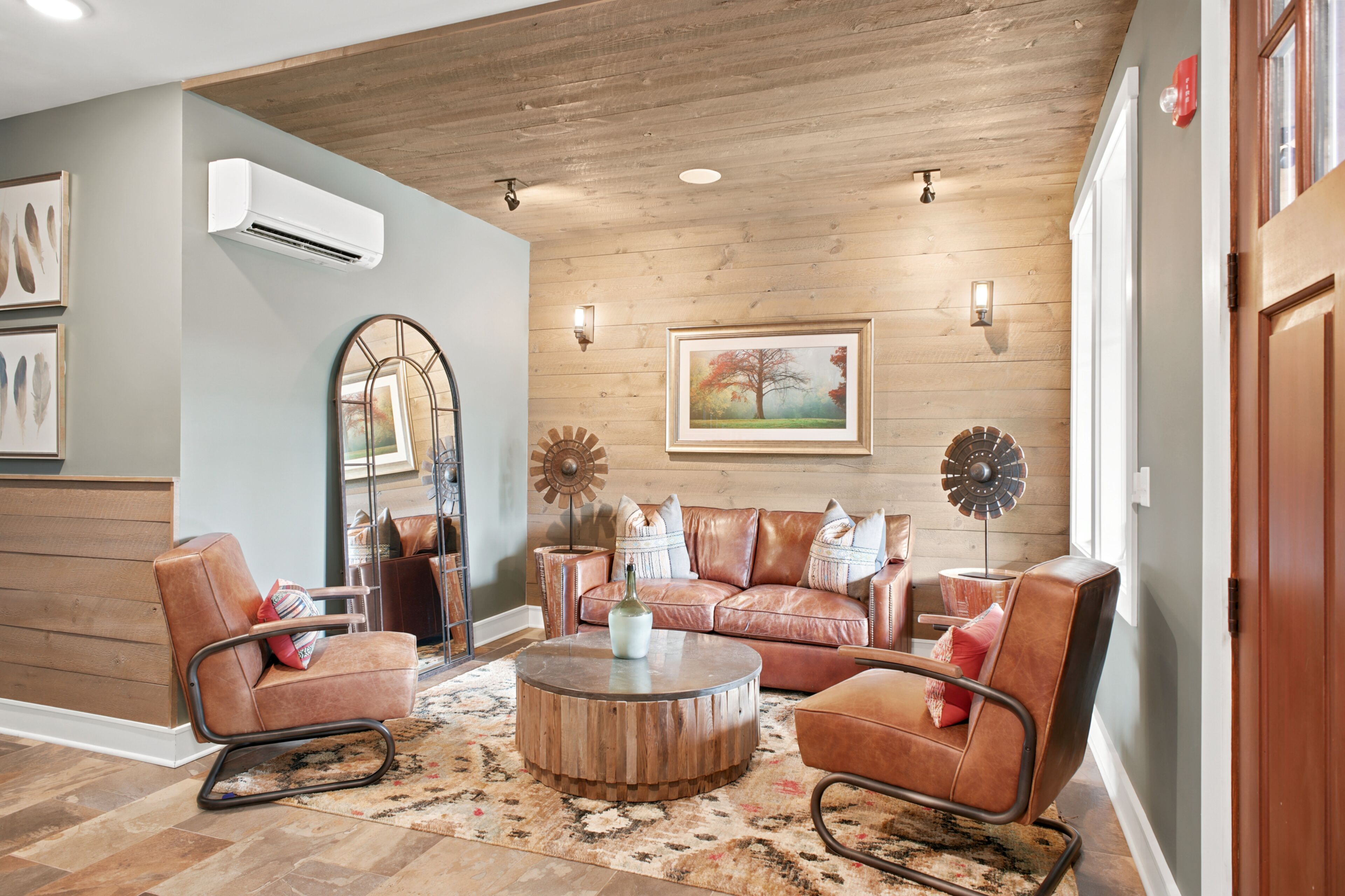 Ein Wohnzimmer mit Holzbalkendecke, einem runden Couchtisch, Ledersofas, einem Ziertegelspiegel und einem gerahmten Gemälde.