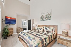 A bedroom with a bed, a television, a painting, and a plant.