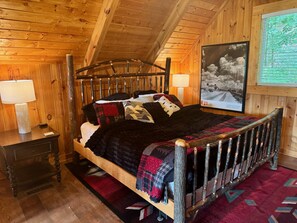 Camera da letto in una baita di legno, con un letto, comodini e una fotografia incorniciata appesa al muro.