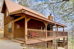 Eine Holzhütte mit Veranda, einem Schild mit der Aufschrift 'Keine Bäume oder Pflanzen entfernen' und einem Willkommensschild.