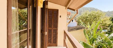 A balcony with a wooden railing, a tiled floor, and a view of greenery and hills.