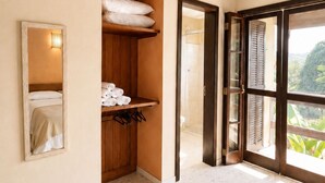 Ett hotellrum med ett träpanelat tak, ett badrum med dusch och ett stort fönster med utsikt över grönområden.