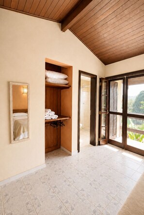 A hotel room with a wooden ceiling, a bathroom with a shower, and a large window offering a view of greenery. - Charming loft with a mezzanine, 2 balconies, and just 10 minutes from the beach (são sebastião)