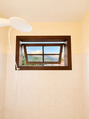 A bathroom with a window, a showerhead, and a view of greenery outside. - Charming loft with a mezzanine, 2 balconies, and just 10 minutes from the beach (são sebastião)