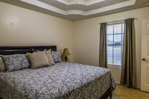 Un dormitorio con cama, mesita de noche, lámpara y ventana con cortinas.
