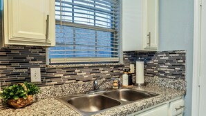 A kitchen with a double stainless steel sink, a window with blinds, and a backsplash made of rectangular tiles. - Cozy Case Mena . Pet Friendly . Fiber WiFi (San Juan)