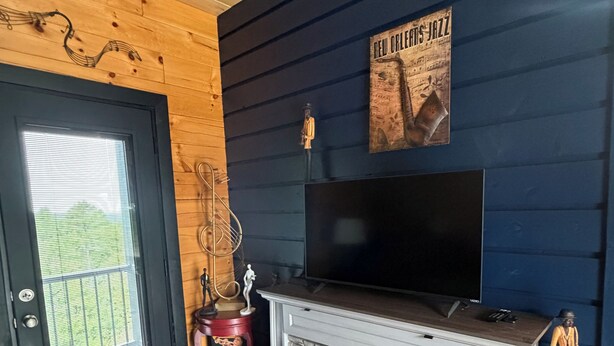 A room with a fireplace, a television mounted above it, and a door with a window. - Jazzy Moon Log Cabin Gorgeous Ozark Mountain Country View No Cleaning Fees (Eureka Springs)