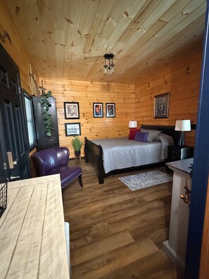 Ein Zimmer mit Holzwandverkleidung, ausgestattet mit einem Bett, einem Schreibtisch, einem Stuhl und einer Lampe.