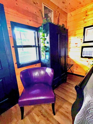 Ein Zimmer mit einem violetten Sessel, einem Holzschrank und einem Fenster mit Jalousien.