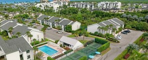 Un complexe résidentiel comprenant plusieurs bâtiments, une piscine, des courts de tennis et offrant une vue sur l’océan.