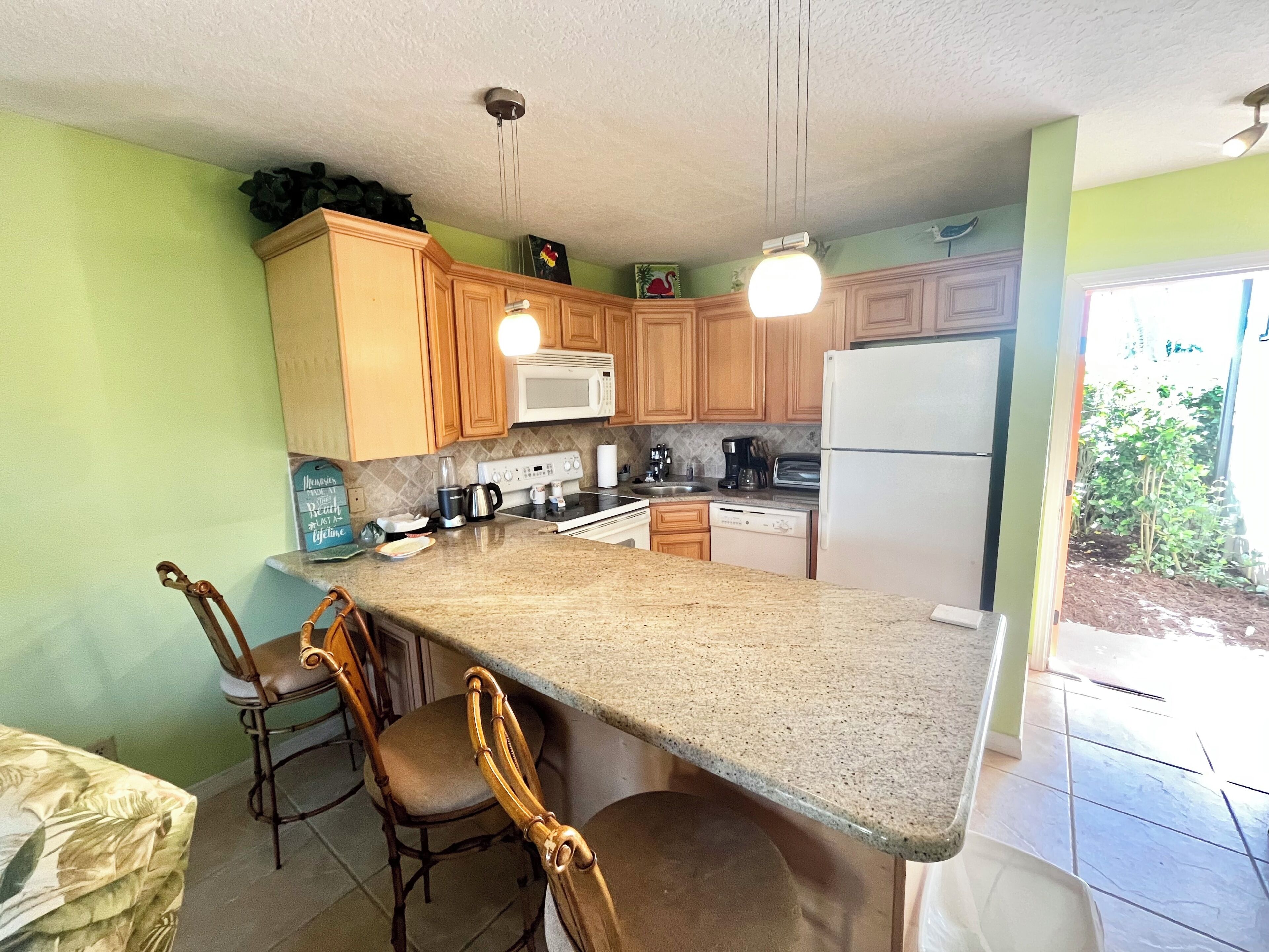 A kitchen with wooden cabinets, a granite countertop, a microwave, a stove, and a refrigerator. There are two chairs and a dining table.