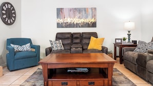A living room with a brown leather sofa, a blue armchair, a wooden coffee table with drawers, a patterned rug, a wall clock, and a painting. - *Scottsdale Kierland*Pool*Spa*Water Fall* (Scottsdale)