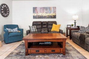 A living room with a brown leather sofa, a blue armchair, a wooden coffee table with drawers, a patterned rug, a wall clock, and a painting. - *Scottsdale Kierland*Pool*Spa*Water Fall* (Scottsdale)